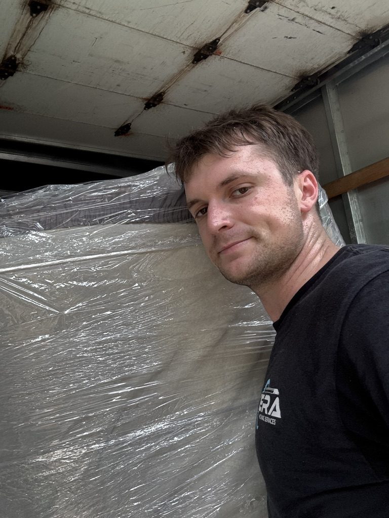 A Tera Moving crew member with a shrink-wrapped mattress loaded in the truck